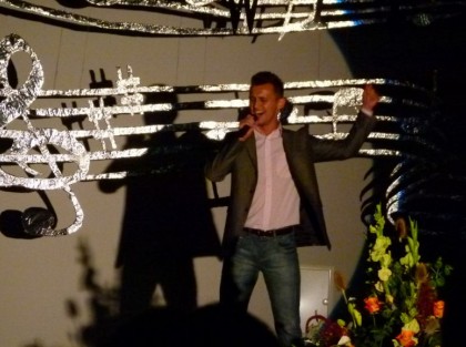 mężczyzna z mikrofonem śpiewa na scenie podczas występu