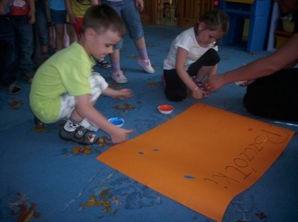 dzieci malujące dużą pomarańczową kartkę na dywanie