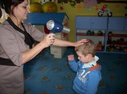 opiekunka dmucha suszarką na włosy chłopca w przedszkolu