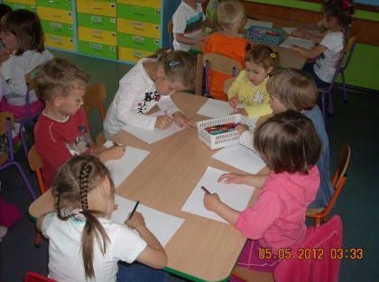 grupa dzieci maluje na kartkach siedząc przy stoliku