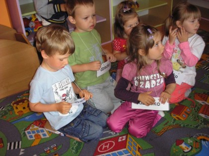 dzieci czytające słowa z kartek w przedszkolu