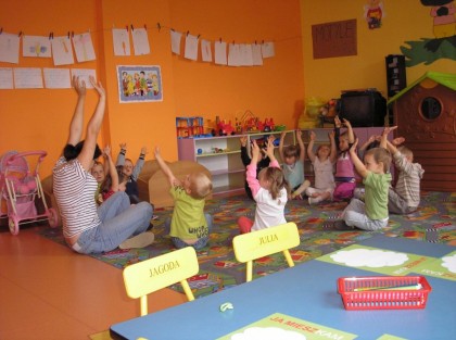 dzieci siedzące na dywanie i trzymające ręce w górze