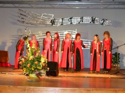 8 kobiet w czerwono czarnych sukniach śpiewa na scenie centrum kultury